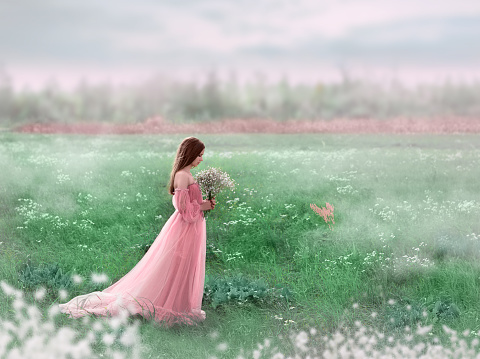 A young girl walks in a field of white flowers. The girl is holding a bouquet in her hands. The girl is wearing a pink long dress.