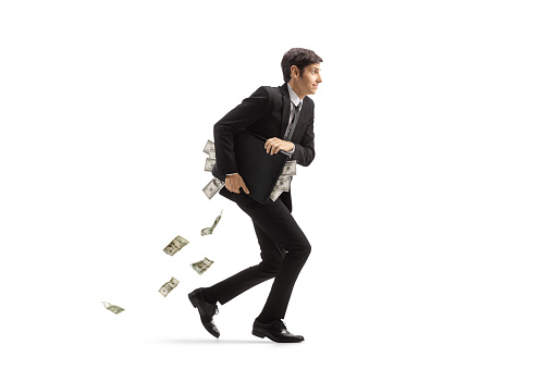 Full length profile shot of a businessman running and holding a briefcase full of money isolated on white background