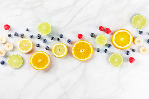 Fresh summer food. Citrus fruit slices, overhead flat lay shot on a white marble kitchen table. Healthy vegan diet with copy space