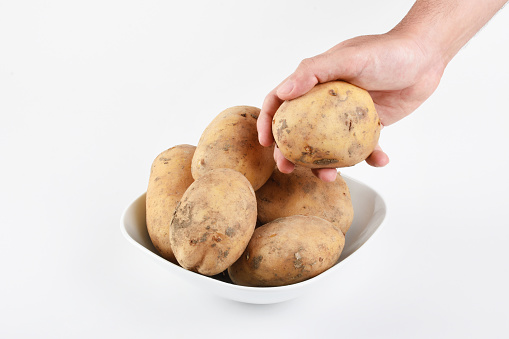 Hand takes a potato from the potato bowl on the white background