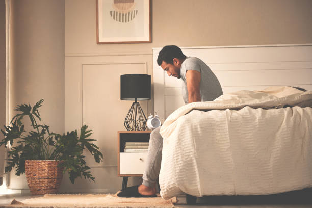 Depressed, stressed man waking up early in morning, sitting in bed and thinking, feeling anxious, nervous and unprepared. Suffering from mental disorder and feeling lost, confused, lonely, detached stock photo
