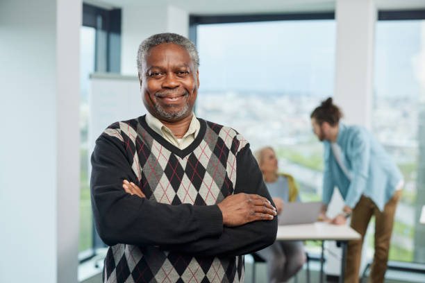 A smiling multicultural senior student is standing with arms crossed in a classroom and looking at the camera. Seniors with bachelor's degree concept. stock photo