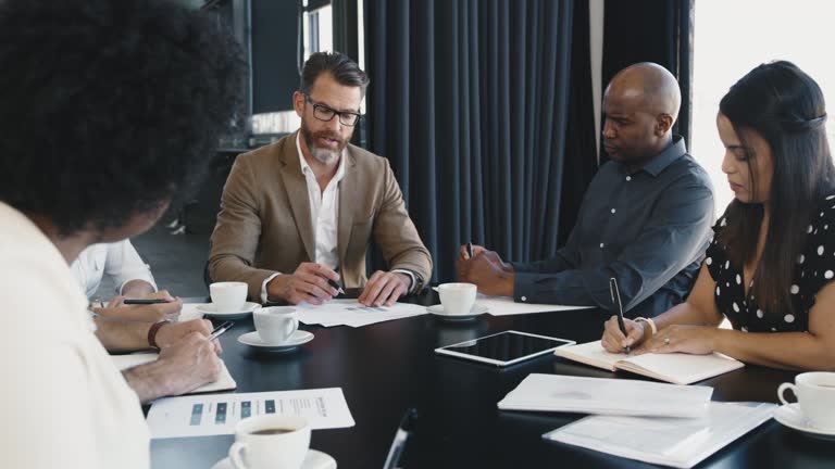 Group of diverse investors in a meeting together talking about investment in a boardroom. Business people brainstorming and planning a strategy while sharing ideas and writing notes with their boss