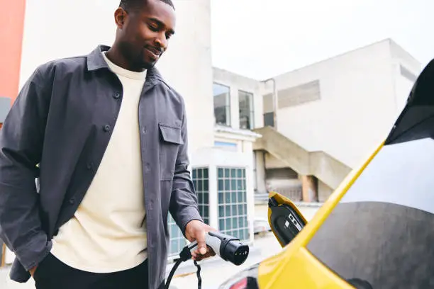 Photo of Man Plugging In Electric Car Outside Office In Car Park Charging