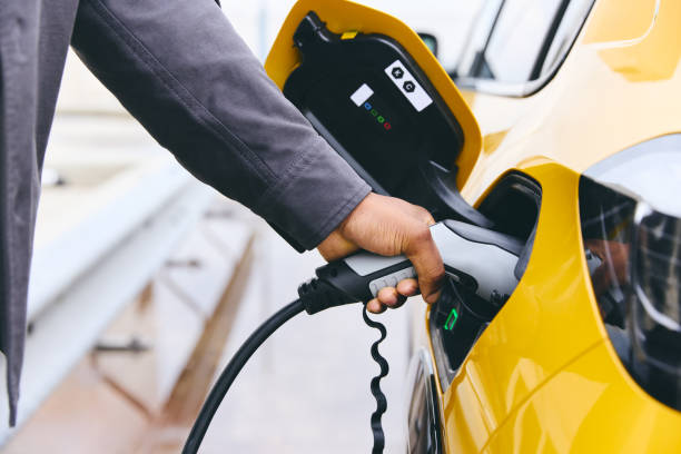 hand plugging in electric car outside office in car park charging - olhar por cima imagens e fotografias de stock