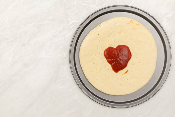 Preparing pizza on the table with ketchup on the top.