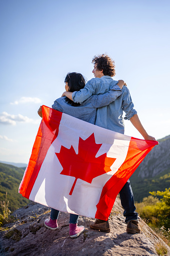 Happy couple holding Canadian national flag on top of the hill