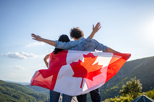 Happy couple holding Canadian national flag on top of the hill