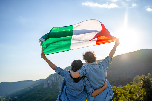 Happy couple holding Italian national flag on top of the hill, rear view