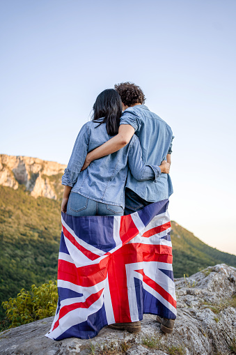 Happy couple holding national flag of United Kingdom on top of the hill, rear view