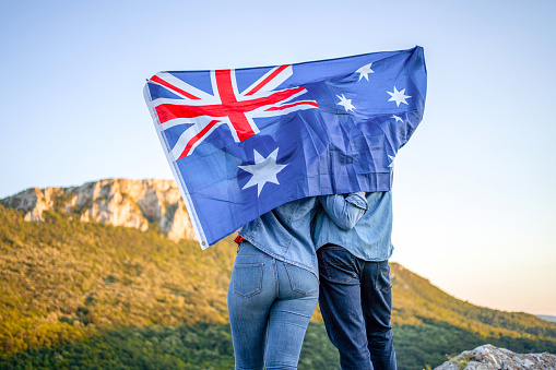 Happy couple holding Australian national flag on top of the hill, rear view