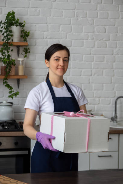 Pastry chef in an apron is holding box with cake for delivery. Selective focus. Photos about confectioners, food, hobbies. stock photo