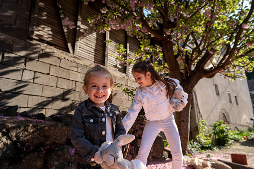 Caucasian sisters playing under tree in blossom, while flower petals falling down