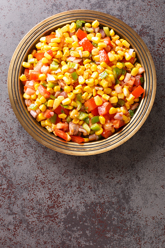 Corn chaat is an Indian snack made using sweetcorn kernels, onions, tomatoes, and a few herbs and spices on a plate closeup on the table. Vertical top view from above