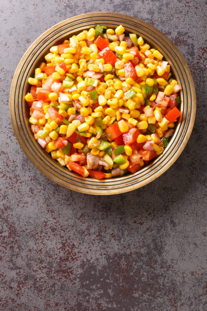 Corn chaat is an Indian snack made using sweetcorn kernels, onions, tomatoes, and a few herbs and spices on a plate closeup. Vertical top view stock photo