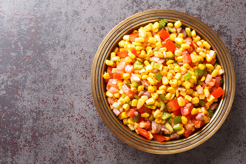 Corn chaat is a super quick snack made with boiled corn, chaat masala, spice powder, onions and tomatoes on a plate closeup on the table. Horizontal top view from above