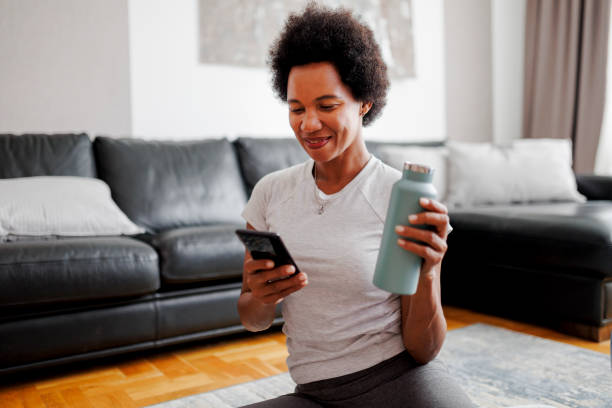 istock Sporty woman drinking water and using her smart phone after home workout 1408402772