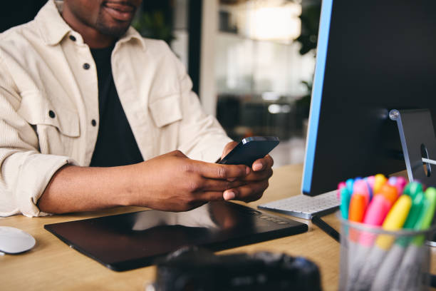 istock Close Up Anonymous Young Black Male Creative In Modern Office Sitting At Desk Using Mobile Phone 1408403715