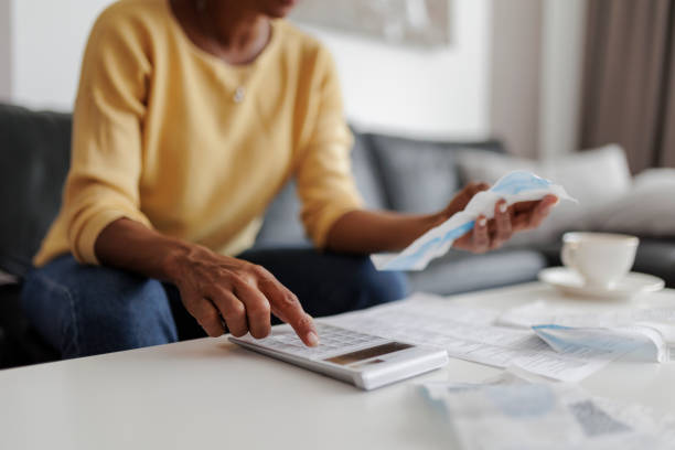 primer plano de una mujer mediana adulta revisando sus facturas de energía en casa, sentada en su sala de estar. ella tiene una expresión preocupada - loan fotografías e imágenes de stock