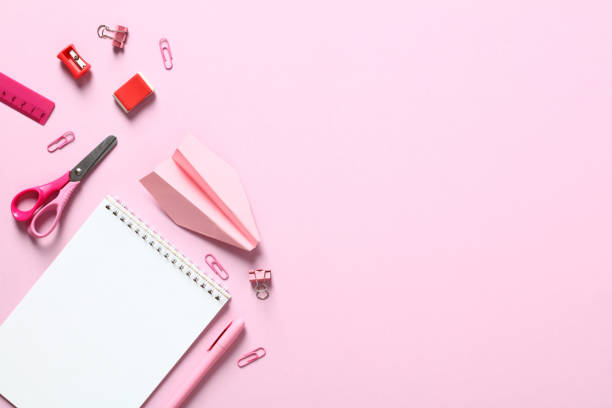 istock Back to school creative layout with notepad, scissors, clips, pen, paper airplane on pink table. Flat lay, top view school supplies. 1408405463