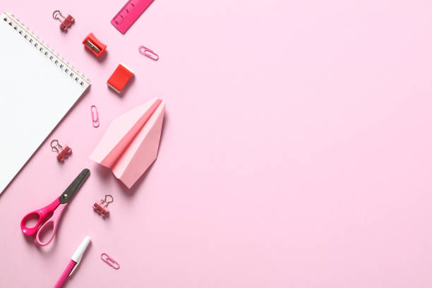 istock Flat lay school supplies on pink background. Top view table with notepad, scissors, clips, pen, paper airplane. Back to school concept. 1408405473