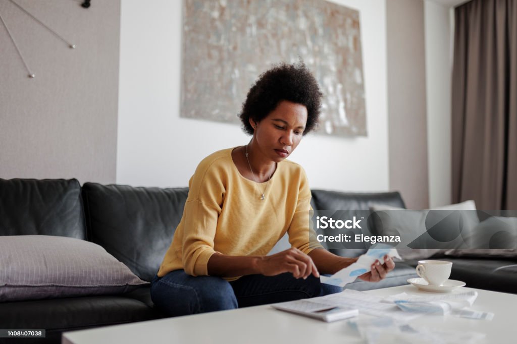 Portrait of a mid adult woman checking her energy bills at home, sitting in her living room. She has a worried expression Inflation - Economics Stock Photo