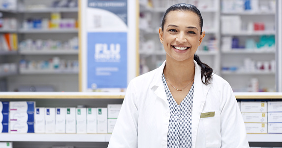 Portrait of trustworthy pharmacist standing against shelves and storage of antibiotics, pills, drugs, painkillers. Friendly healthcare professional ready to assist and help. Over the counter relief