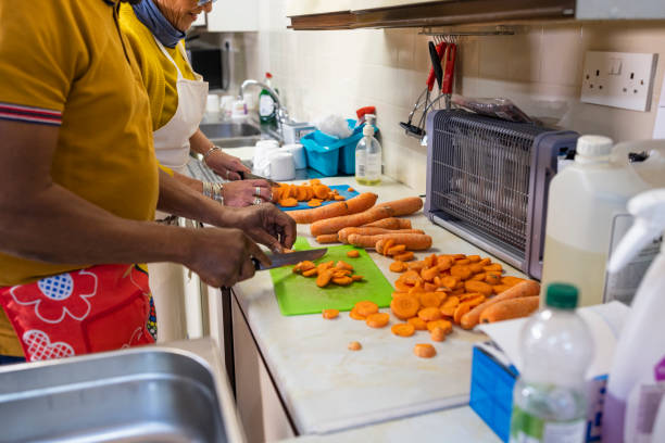 Side view medium shot of volunteers working in a soup kitchen/food bank preparing food in the North East of England. They are chopping carrots together.