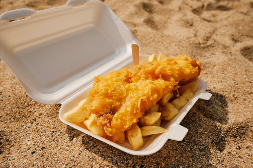 Carton of Fish and Chips on the sand at the beach, Newquay, Cornwall on a sunny June day.