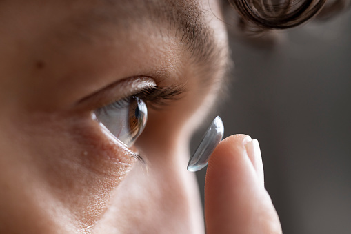 Extreme close up of a young male adult holding a contact lens getting ready to insert into his eye with his finger.