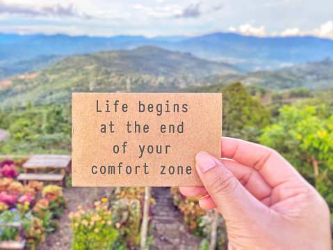 Inspirational motivating quote - life begins at the end of your comfort zone. Text on paper with nature background.