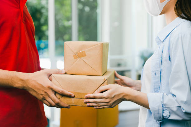 close up delivery man in red uniform deliver service parcel box to customer woman at home stock photo