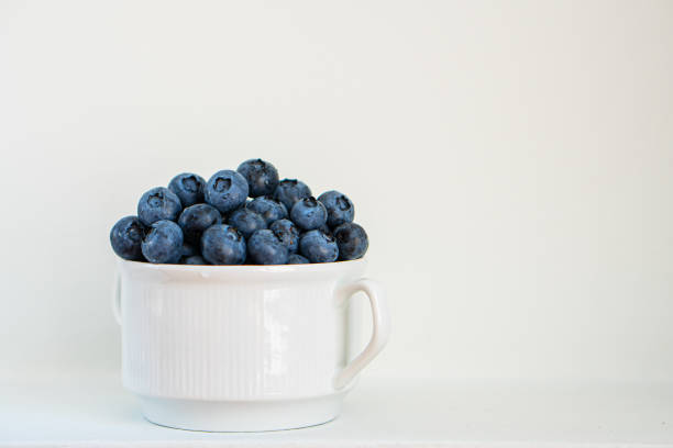 Water drops on ripe blueberries in small white dish on gray background.