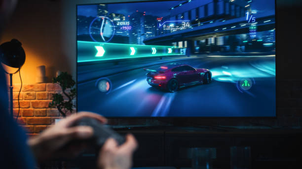 acércate a las manos del hombre en casa, siéntate en un sofá en un elegante apartamento loft y juega videojuegos de autos arcade en consola. macho usando el controlador para jugar street racing drift simulator. - street racing fotografías e imágenes de stock