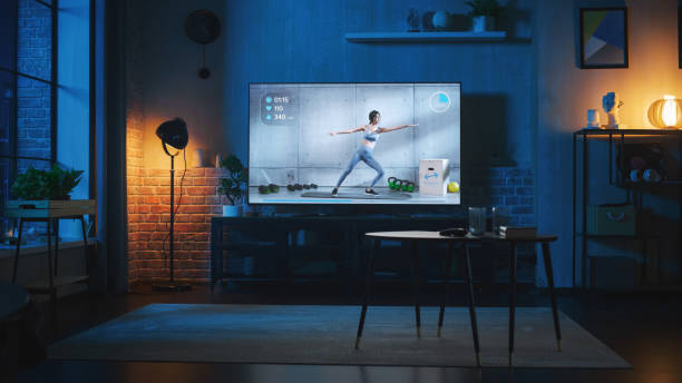 stilvolles loft-apartment-interieur mit online-fitness-anwendung, die auf smart-tv-gerät spielt. leeres wohnzimmer zu hause mit professionellem fitnesstrainer, der bewegungen auf flachbildfernseher zeigt. nachtaufnahme. - fernsehstudio stock-fotos und bilder