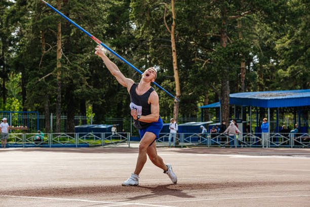 man athlete about to throw a javelin in the stadium. sportsman practising javelin throw against bright blue sky with clouds