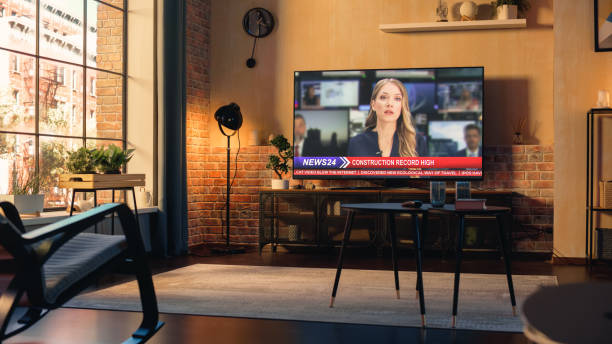 istock Stylish Loft Apartment Interior with Television News Program Playing. Empty Living Room at Home with TV Set Broadcasting Local News Chanel. Beautiful Female Host Talks. Sunset Warm Shot. 1408421610