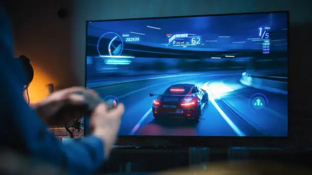 Close Up on Man's Hands at Home, Sitting on a Couch in Stylish Loft Apartment and Playing Arcade Car Video Games on Console. Male Using Controller to Play Street Racing Drift Simulator.