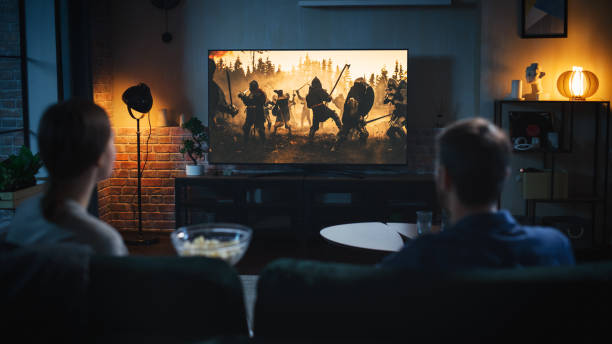 authentic couple spending time at home, sitting on a couch and watching latest blockbuster on flat screen television set. man and woman streaming movie or show using home cinema system. - canal imagens e fotografias de stock