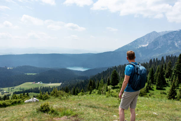 istock Young man hiking looks at mountain lake 1408424070