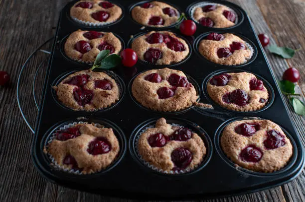 Fresh and homemade baked muffins with sour cherries. Served hot in a muffin pan isolated on wooden table background.