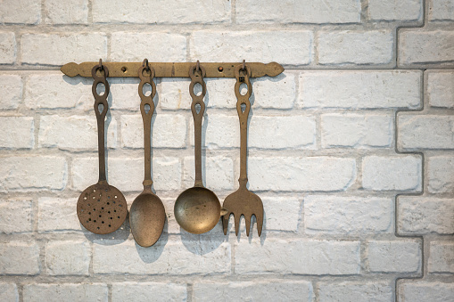 Set of antique style kitchen untensils which are handing on white brick wall, Interior decoration object photo. Selective focus.