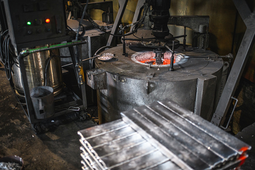 Aluminium ingots and crucible furnace in a metallurgy plant. Heavy duty machinery.