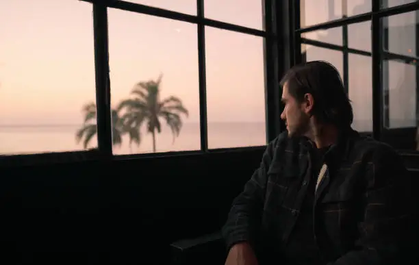 young hispanic man looks out the window in a bar at sunset