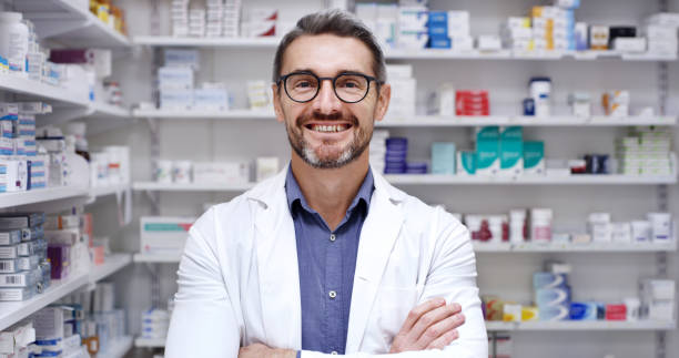 dojrzały mężczyzna pracujący w aptece. portret pewnego siebie uśmiechniętego kierownika farmaceutycznego i pracownika służby zdrowia stojącego ze skrzyżowanymi rękami, gotowego pomóc klientom z lekami w aptece - pharmacy pharmacist smiling pill zdjęcia i obrazy z banku zdjęć
