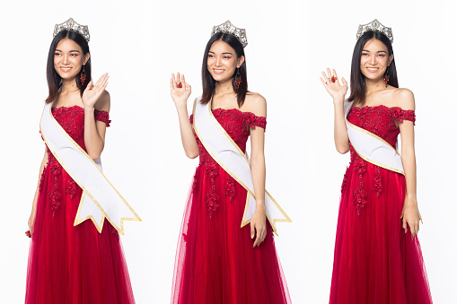 Half body of Miss Beauty Pageant Contest wear red evening sequin gown with diamond crown sash, Asian female stand express feeling happy smile over white background isolated