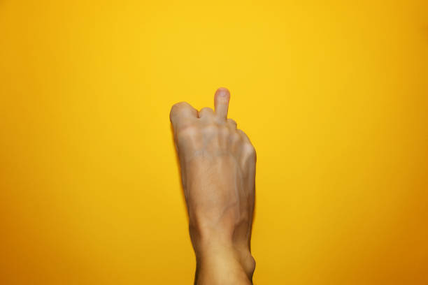 Middle finger on the leg, an offensive gesture. Funny concept Fuck you. The male foot shows the sign Fuck you. Top view on a yellow background. stock photo