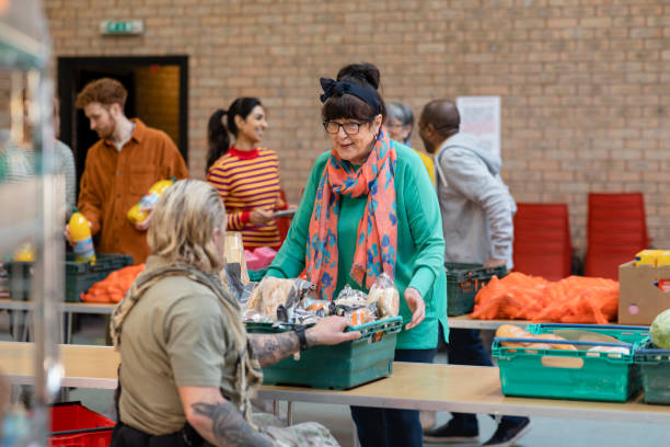 Food Drive at a Church Group of volunteers organising food donations onto tables at a food bank in the North East of England. They are working together, setting up sections of the room in a church. cost of living stock pictures, royalty-free photos & images