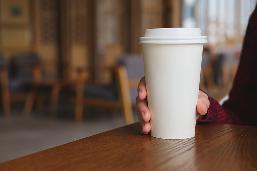 Woman hand holding coffee cup on wooden table in coffee cafe.