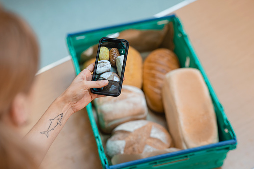 Focus on the screen of a mobile phone while an unrecognisable person takes a photo of fresh bread ready to be given out at a food bank in the North East of England.